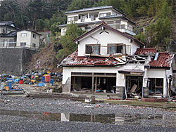 石巻市の月の浦では、今でも満潮時は冠水し、高台にある避難所の民家に入るには潮が引くのを待つしかない状態です。。